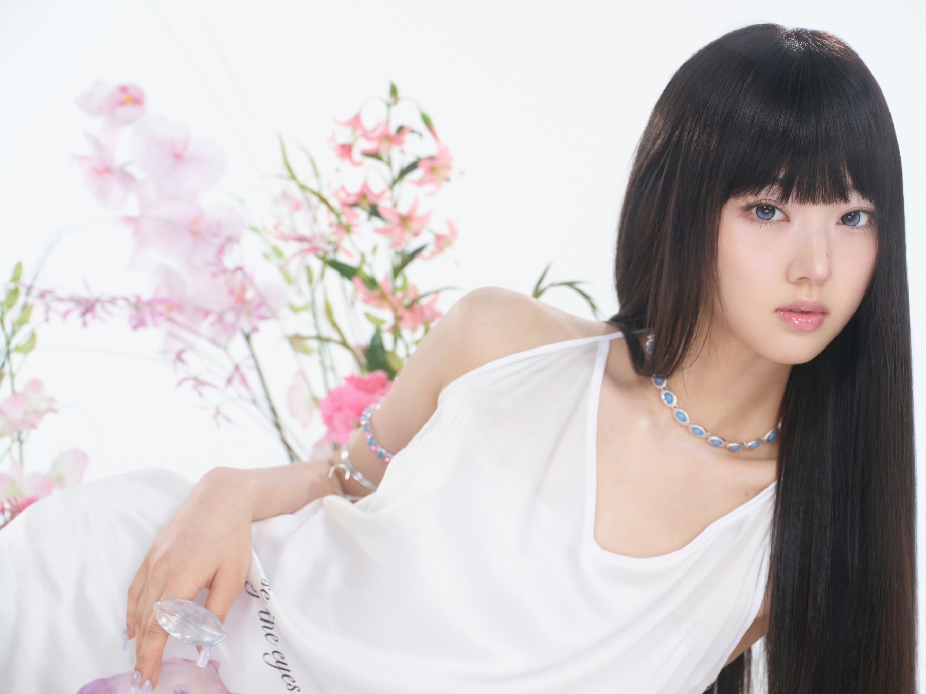 A K-pop performer in white posed against a bright floral background.