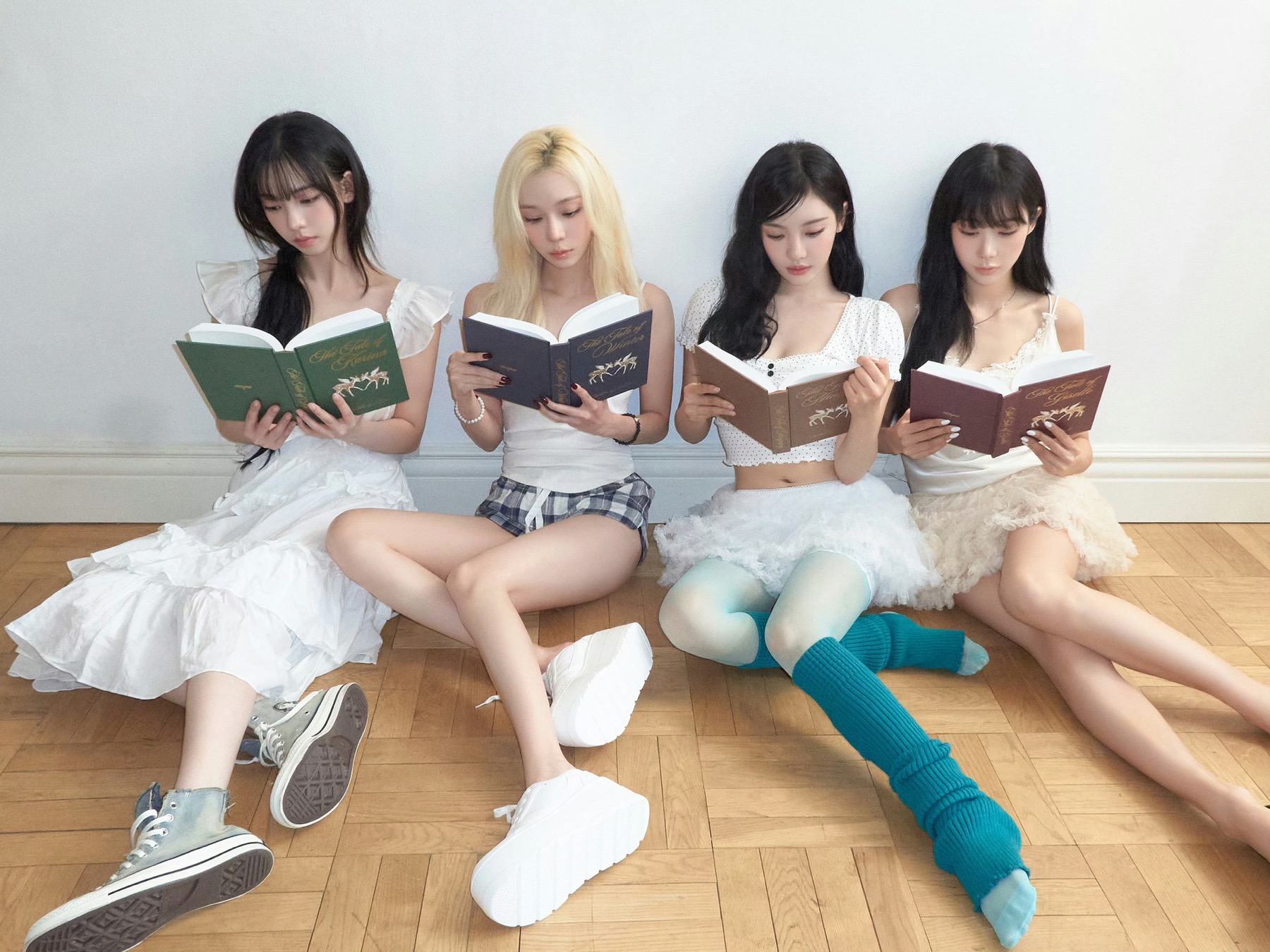 Four members of aespa seated together reading books in a bright room.