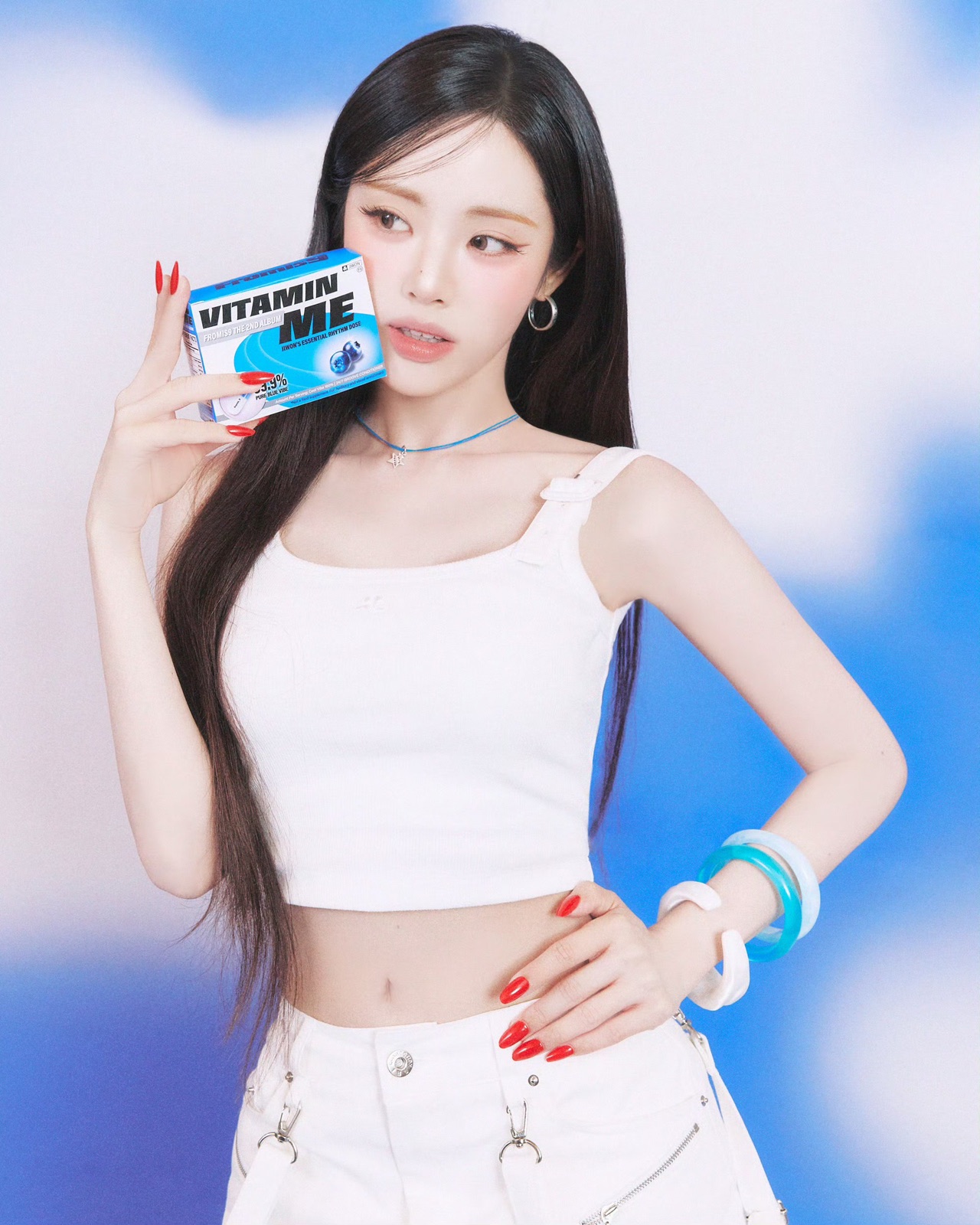 A fromis_9 member holding a blue Vitamin Me package against a blue and white background.