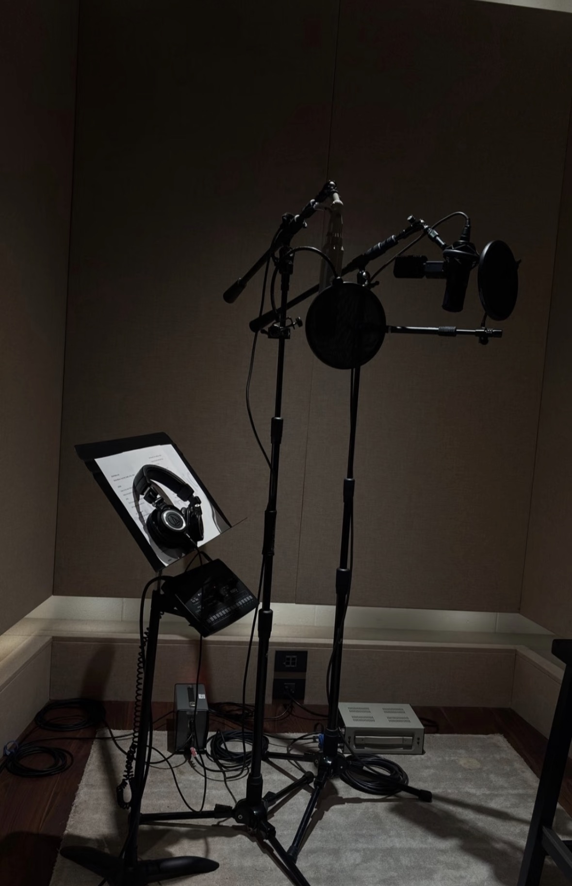 A dimly lit recording booth with microphones, pop filters, headphones and recording equipment.
